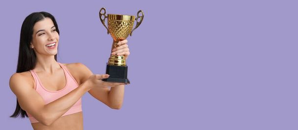 Sportieve jonge vrouw met trofee beker op lila achtergrond met ruimte voor tekst - Foto, afbeelding