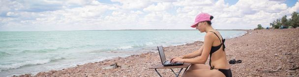 dziewczyna w seksownym stroju kąpielowym pracująca przy stole na oceanie, pracująca zdalnie z biura, - Zdjęcie, obraz