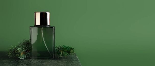 Botella de perfume y ramas de coníferas sobre fondo verde con espacio para texto - Foto, imagen