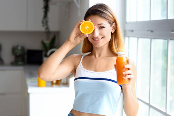 Jonge vrouw met sinaasappel en glas sap in keuken - Foto, afbeelding