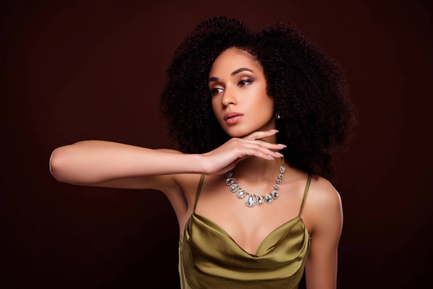Portret van aantrekkelijke vrouw touch kin sieraden reclame gekleed stijlvolle zijdeachtige kleding geïsoleerd op bruine kleur achtergrond. - Foto, afbeelding