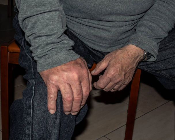 Le mani della persona caucasica anziana che effettuano aggiustamenti alla vestibilità dei jeans blu indossati - Foto, immagini