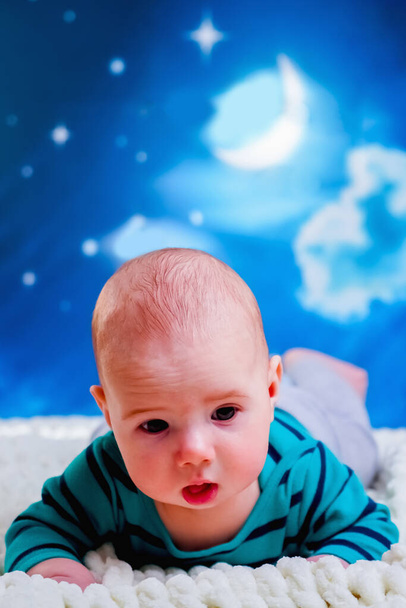 Ideje aludni, gondtalan álmok koncepciója. Vicces portré a kisfiú 4 hónapos fekszik az ágyon szemben éjszakai égbolt háttér. Függőleges kép. - Fotó, kép