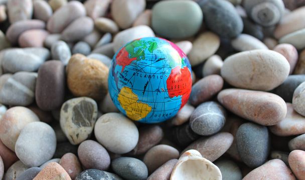 Миниатюрный глобус на морских камнях с традиционно нарисованными континентами, океанами и торговыми путями на нем - Фото, изображение