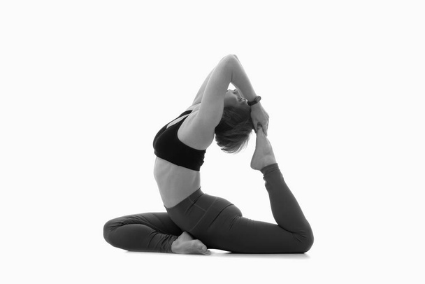 Königstaubenpose, Ashtanga Yoga Seitenansicht einer Frau in Sportkleidung, die Yoga-Übungen vor weißem Hintergrund macht. Schwarz-Weiß-Bild. - Foto, Bild