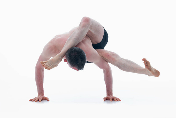 Eka pada sirsasana. (Одна нога на голове), человек, занимающийся йогой в штанах, делает упражнения йоги на белом фоне. Горизонтальное изображение. - Фото, изображение