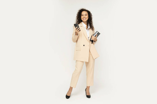 Приваблива бізнес-леді в костюмі зі смартфоном і книгами в руках - Фото, зображення