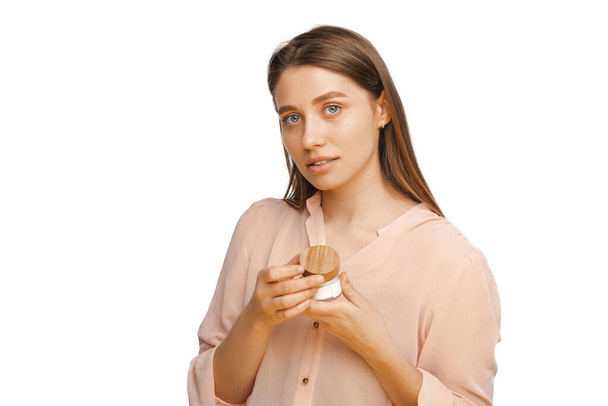 Στιγμιότυπο μιας νεαρής γυναίκας που κρατάει ένα βάζο με κρέμα προσώπου κοιτάζοντας την κάμερα.. - Φωτογραφία, εικόνα