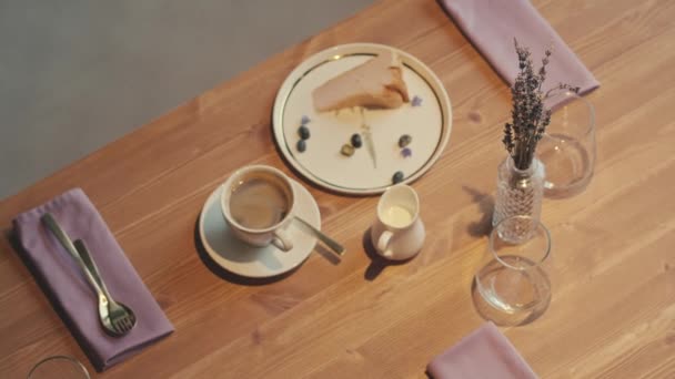 Nincs ember felvételeket fa asztal kávézó csésze kávé, tej kancsó és egy darab sajttorta tányéron mellett ágak örök virágok üveg vázában - Felvétel, videó