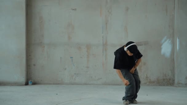 Kulaklıktan çimento arka planda müzik dinlerken break dans pratiği yapan yakışıklı bir hippi. Sokak dansçısının hareketli çekimi robot dansı yapar. Açık hava sporu 2024. Modern dans. hiphop. - Video, Çekim