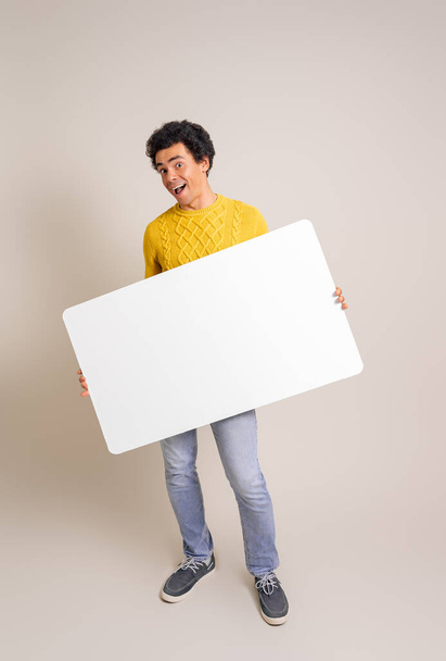 Retrato del joven vendedor alegre que muestra la bandera blanca en blanco mientras que hace publicidad en el fondo blanco - Foto, Imagen