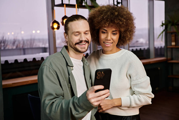 Un hombre y una mujer afroamericana absortos en un teléfono celular en un café moderno. - Foto, Imagen