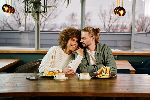 Une femme afro-américaine et un homme dégustant un repas ensemble à une table dans un café moderne. - Photo, image