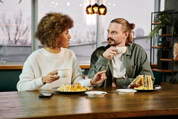 Eine afroamerikanische Frau und ein Mann genießen ein gemeinsames Essen an einem Tisch in einem modernen Café. - Foto, Bild