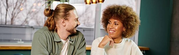 Een Afro-Amerikaanse vrouw en een man die naast elkaar zitten in een modern café, in gesprek zijn en koffie drinken. - Foto, afbeelding