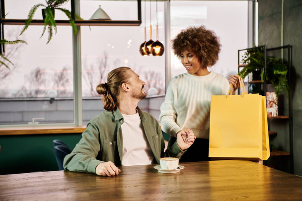 Zwei stylische Frauen, eine Afroamerikanerin, sitzen an einem Tisch mit einer Einkaufstasche, plaudern und bewundern ihre neuen Einkäufe. - Foto, Bild