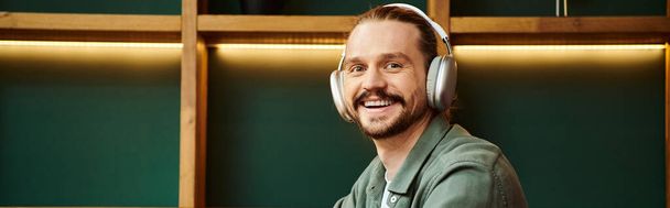 happy man sitting at a table, engrossed in music with headphones in cafe - Photo, Image