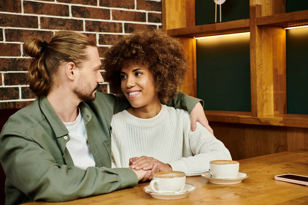 An African American woman and man sit at a table, enjoying cups of coffee in a modern cafe setting. - 写真・画像
