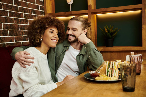 Um homem e uma mulher de ascendência afro-americana sentam-se juntos a uma mesa em um café moderno, envolvidos em conversas.. - Foto, Imagem