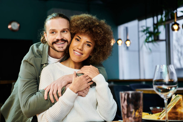Μια Αφροαμερικανή γυναίκα και ένας άντρας μοιράζονται μια τρυφερή αγκαλιά σε ένα μοντέρνο καφέ σκηνικό.. - Φωτογραφία, εικόνα