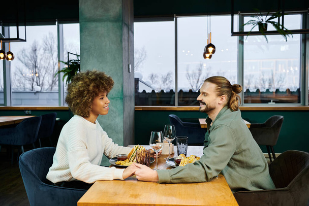 Una donna afroamericana e un uomo si godono un pasto insieme in un caffè moderno, impegnati in conversazioni e risate.. - Foto, immagini
