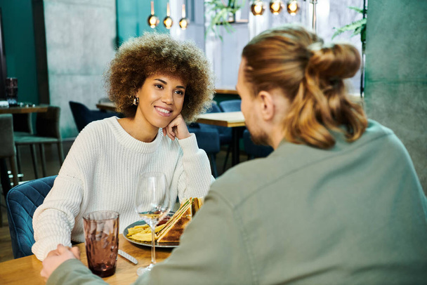 Элегантная афроамериканка сидит за столом с прекрасно приготовленной тарелкой еды в современном кафе. - Фото, изображение