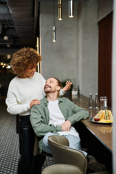 Eine afroamerikanische Frau und ein Mann sitzen zusammen in einem modernen Café, unterhalten sich und fühlen sich in der Gegenwart des jeweils anderen wohl.. - Foto, Bild