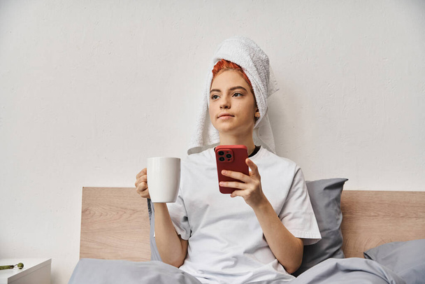 positiivinen rentouttava homo henkilö homewear hiukset pyyhe puhelimitse ja juo teetä sängyssä - Valokuva, kuva
