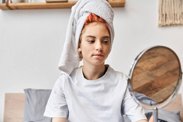atractiva persona extravagante con toalla de pelo blanco mirando en el espejo durante la rutina de la mañana en casa - Foto, Imagen