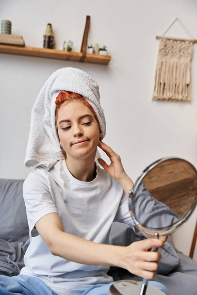 ελκυστικό υπερβολικό πρόσωπο με λευκή πετσέτα μαλλιών κοιτάζοντας στον καθρέφτη κατά τη διάρκεια της ρουτίνας πρωί στο σπίτι - Φωτογραφία, εικόνα