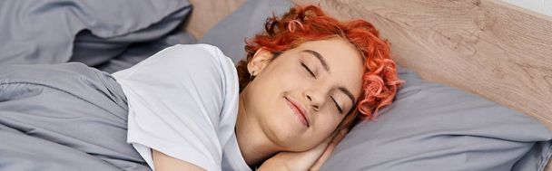 gut aussehende rothaarige queere Person in Hauskleidung, die zu Hause im Bett schläft, Freizeit, Banner - Foto, Bild