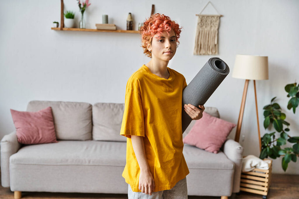 sporty young queer person with red hair in vibrant attire holding yoga mat and looking at camera - Photo, Image