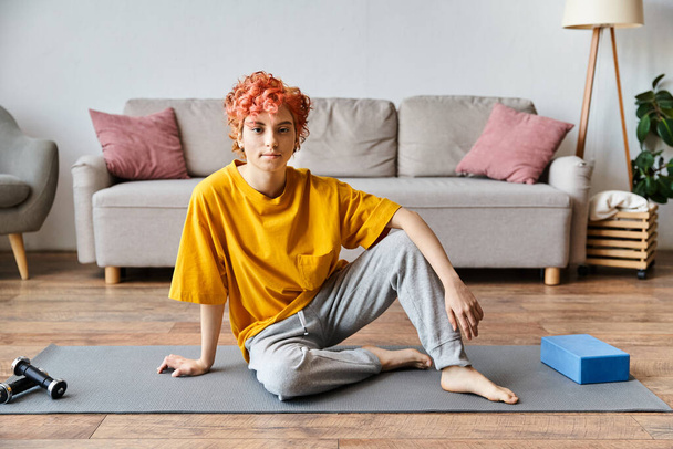 beautiful queer person in vibrant yellow t shirt sitting on yoga mat and looking at camera - Photo, Image