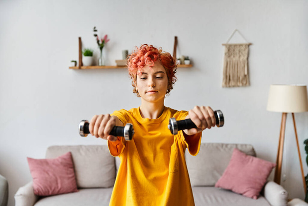 appealing young queer person in vibrant sport attire exercising with dumbbells while at home - Photo, Image