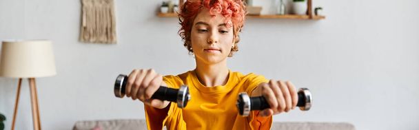 good looking queer person in vibrant sport attire exercising with dumbbells while at home, banner - Photo, Image