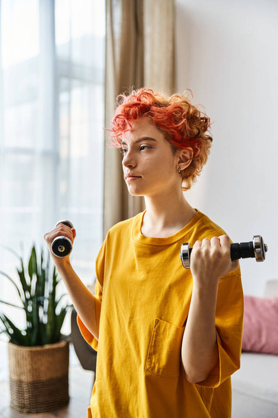 attractive young queer person in vibrant sport attire exercising with dumbbells while at home - Photo, Image