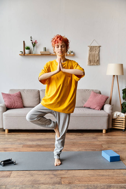 aantrekkelijk rood haar queer persoon in levendige outfit mediteren met gesloten ogen terwijl thuis - Foto, afbeelding