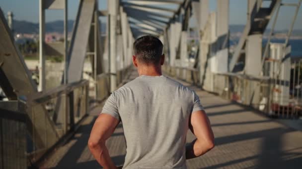 Folgen Sie dem Rücken eines nicht wiederzuerkennenden reifen starken Mannes, der allein auf einer modernen städtischen Brücke läuft, disziplinierter Mann bleibt fit und fest und verbrennt Kalorien für einen gesunden Körper. Menschen, die täglich Cardio-Sport treiben - Filmmaterial, Video