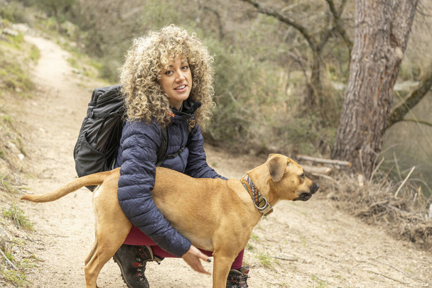Kręcone włosy i kobieta alpinistka i jej pies pozowanie na świeżym powietrzu podczas spaceru po górach. - Zdjęcie, obraz