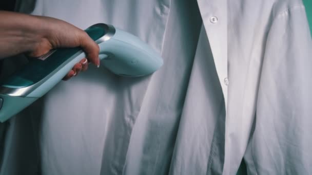 Handheld Steam Iron Smoothing White Shirt retrata um ferro a vapor em ação, removendo rugas de uma camisa branca para um olhar nítido. - Filmagem, Vídeo