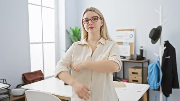 Selbstbewusste junge blonde Frau mit Brille steht mit verschränkten Armen in einem modernen Büro. - Filmmaterial, Video