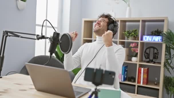 Podekscytowany młody Hiszpan w słuchawkach zdobywa duże zwycięstwo w studiu radiowym! radosne zwycięstwo krzyk sukcesu, pewny siebie gest zwycięzcy - Materiał filmowy, wideo