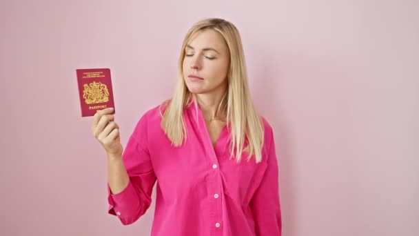 Femme blonde confiante pointe son doigt vers vous et vers son passeport d'Irlande du Nord, donnant un regard sérieux à la caméra sur un fond rose isolé - Séquence, vidéo