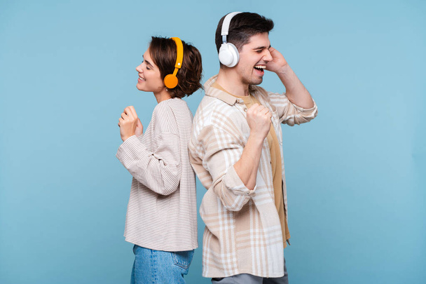Νεαρό διασκεδαστικό ζευγάρι δύο φίλοι οικογένεια άντρας γυναίκα φορούν casual ακουστικά ρούχα ακούγοντας μουσική, τραγούδι μαζί απομονώνονται σε μπλε φόντο στούντιο  - Φωτογραφία, εικόνα