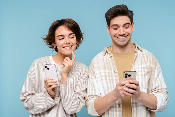 Donna sorridente guardando smartphone del suo ragazzo isolato su sfondo blu. Amici felici in possesso di telefoni cellulari, comunicazione online. Tecnologia, concetto di dipendenza dai social media  - Foto, immagini
