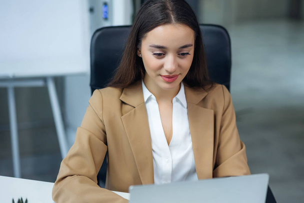 Moderna empresaria de oficina sentada en su escritorio trabajando en una computadora portátil. Sonriente mujer exitosa trabajando en el cargo - Foto, Imagen