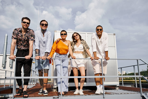 joyous young multicultural friends in casual urban attires posing on rooftop and looking at camera - Фото, изображение