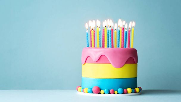 Gâteau d'anniversaire coloré avec beaucoup de bougies d'anniversaire et glaçage goutte à goutte sur un fond bleu - Photo, image
