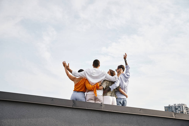 back view of group of young multicultural friends in casual urban attires hugging on rooftop - Photo, Image