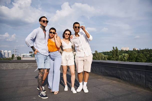 four multicultural jolly friends with modern sunglasses posing happily on rooftop together - Foto, imagen